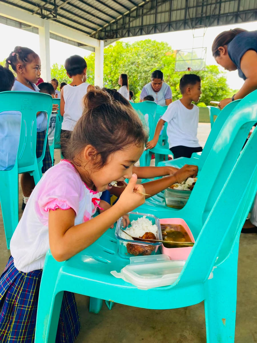 A girl eating a spoonful of rice from a container balanced on a green plastic chair.