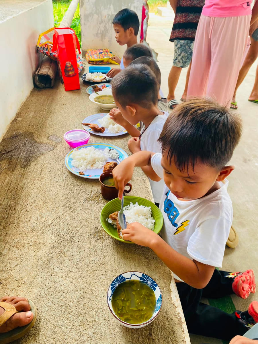 Young boys eating rice, chicken and mongo stew from bowls set along a low concrete ledge.