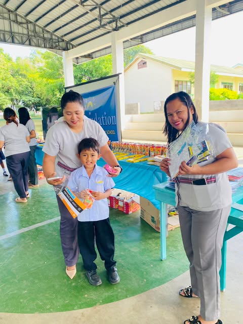 A teacher and a parent standing with a young student in uniform as he receives his new school supplies.